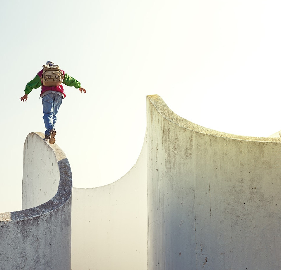 brave extreme man with backpack walking on a thin concrete wall